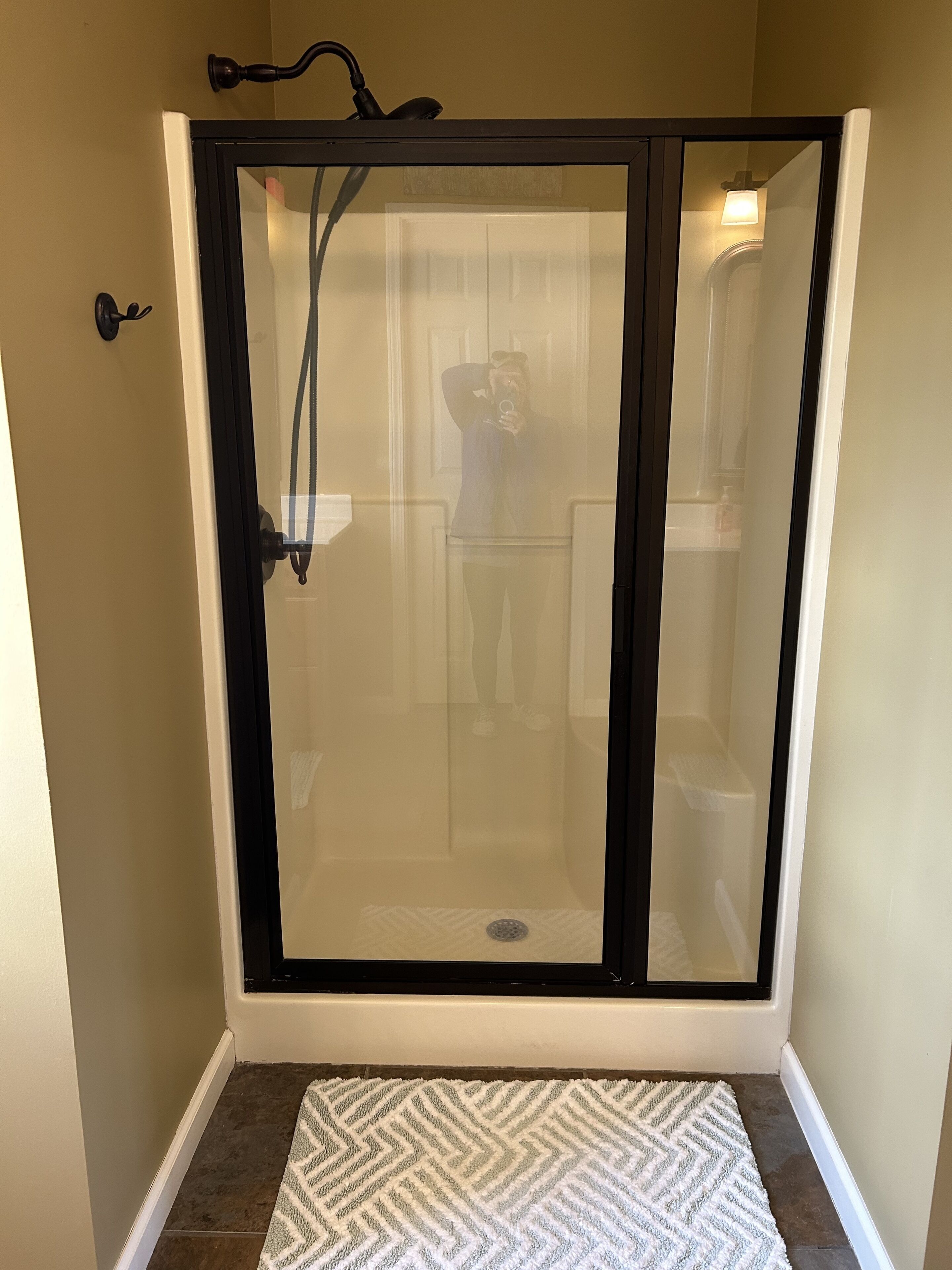 A walk-in shower with a glass door, a showerhead, and a white rug at the entrance.