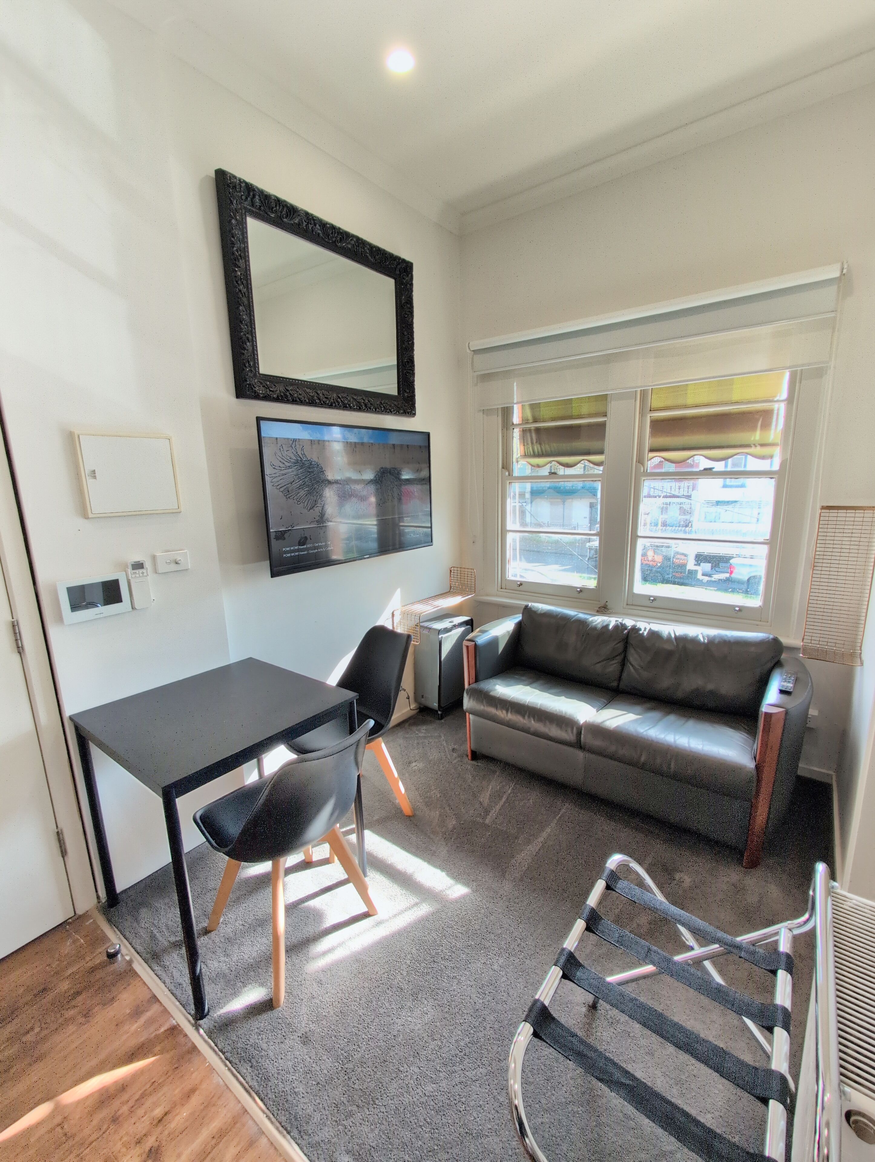 A compact living space with a sofa, a dining table, a chair, a radiator, and a window with blinds.
