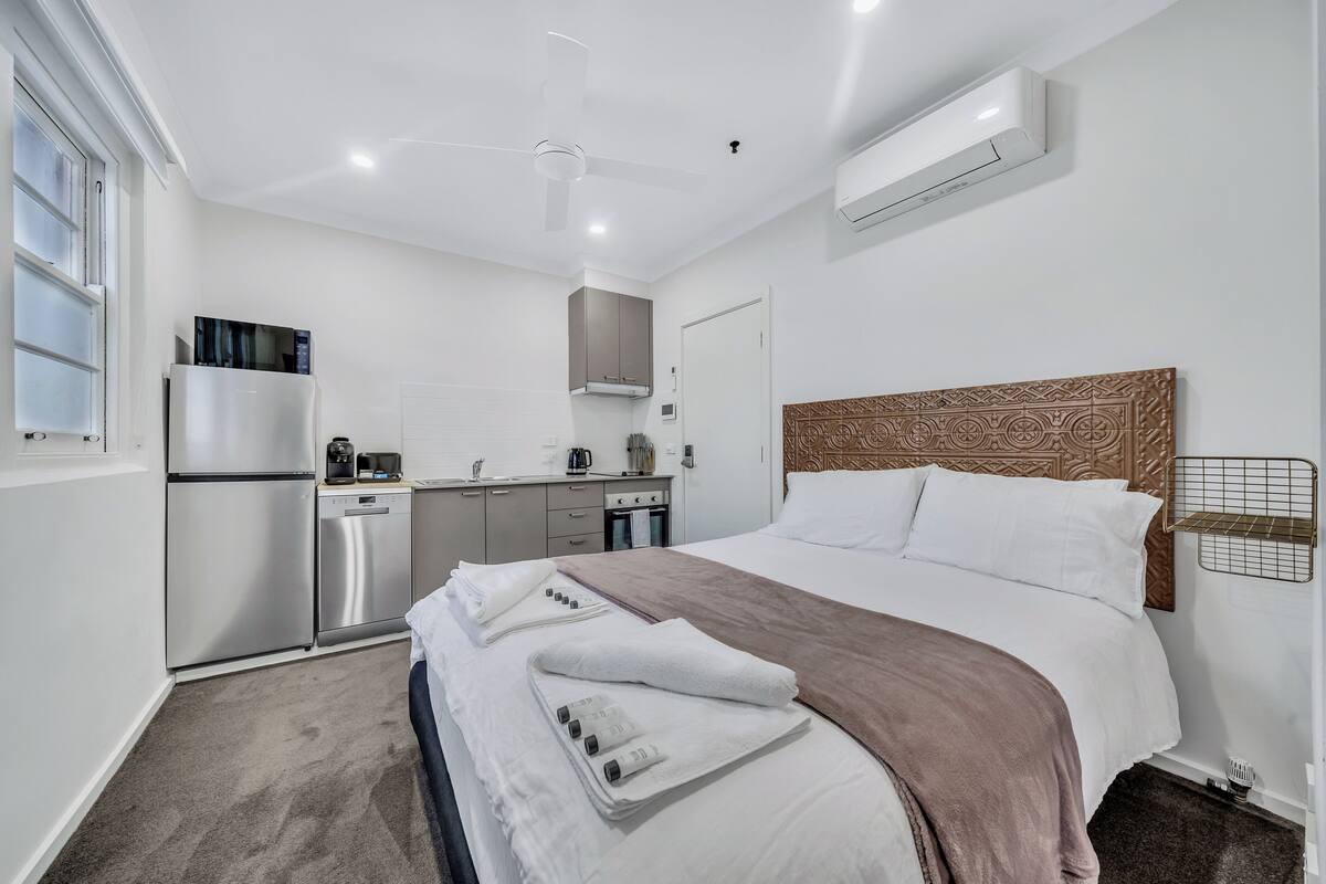 A modern hotel room with a bed, a kitchenette, and a ceiling fan.