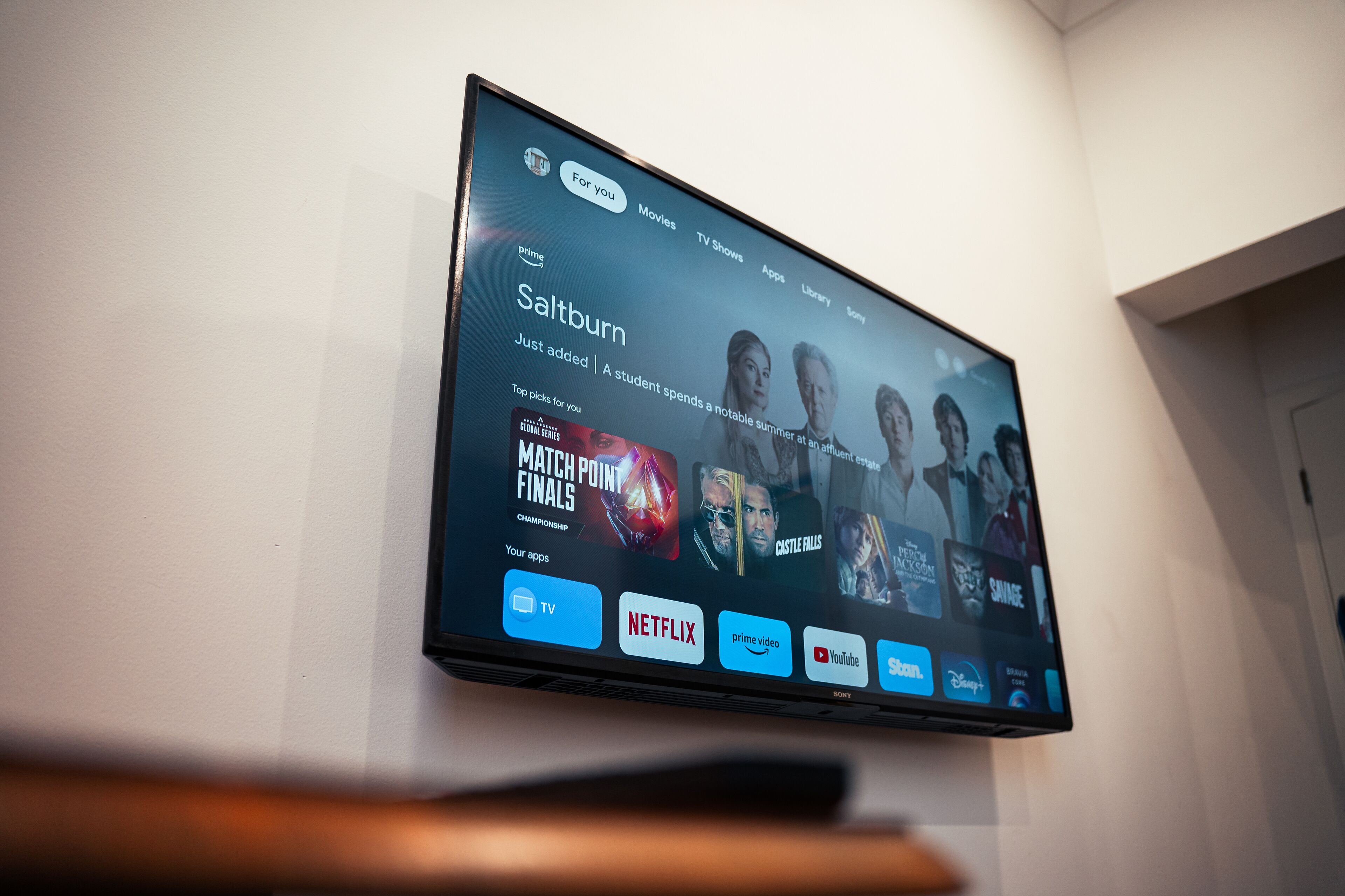 Un téléviseur à écran plat fixé au mur affiche l’interface d’un service de diffusion en continu, proposant différentes options de contenu.