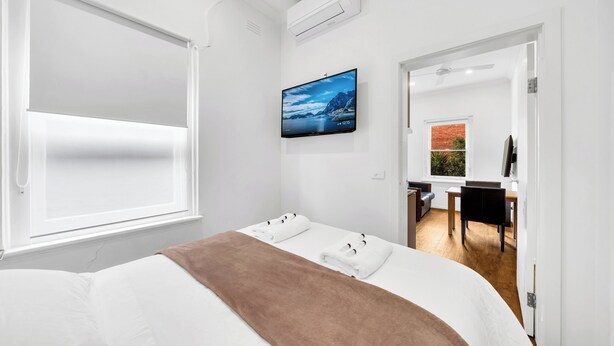 Una camera d'albergo con un letto, una TV a muro e una finestra con persiane.