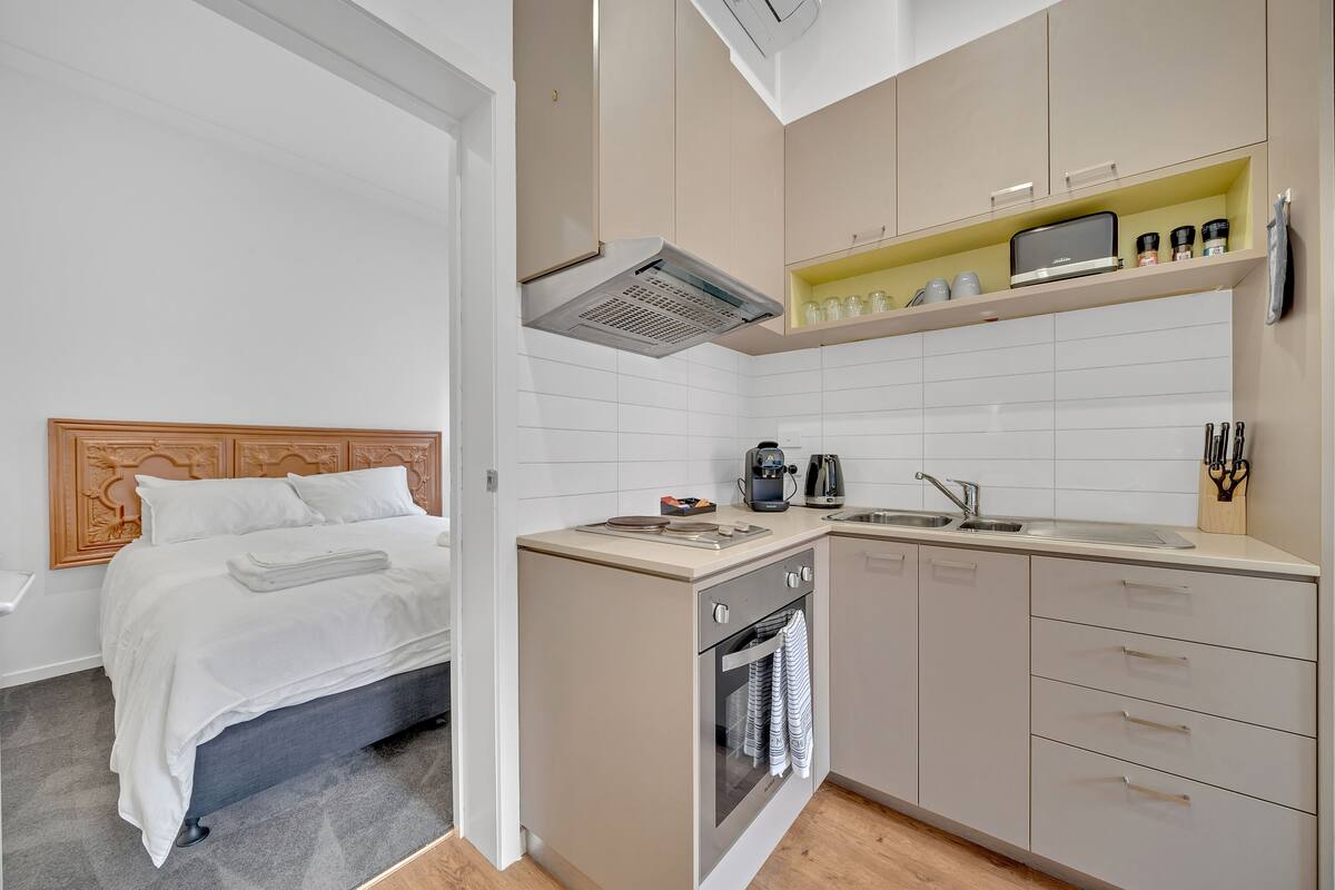 A compact hotel room with a bed, kitchenette, and a small bathroom.