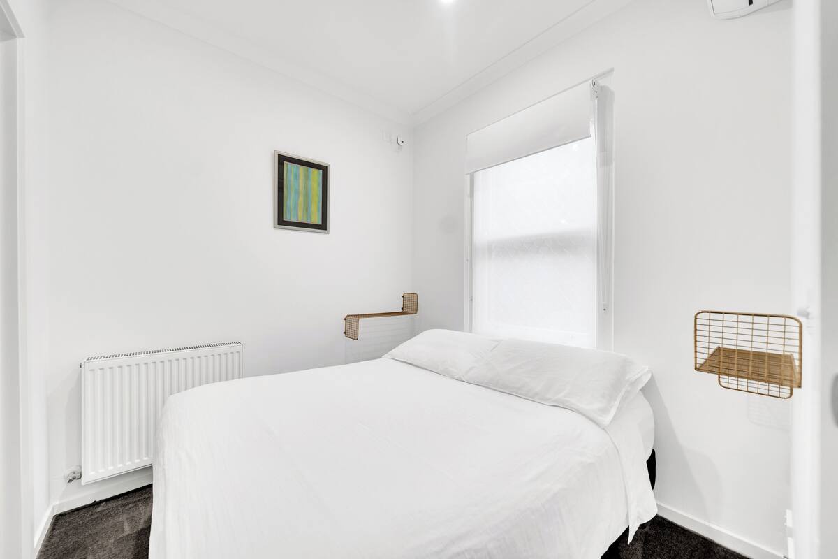 A bedroom with a bed, a radiator, a window, and a picture on the wall.