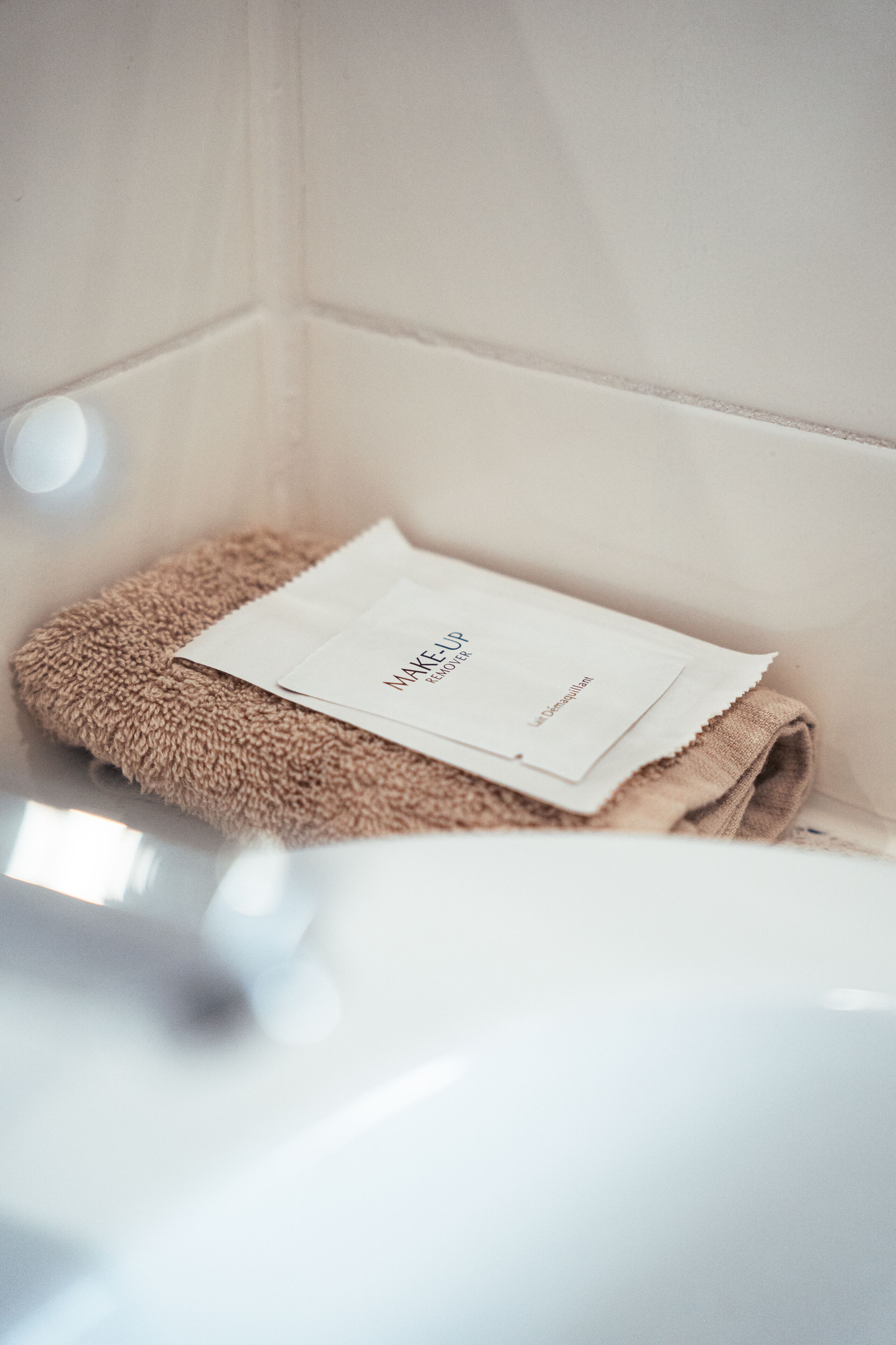 Un baño con una toalla color beige y una caja de pañuelos blancos sobre un lavamanos blanco.