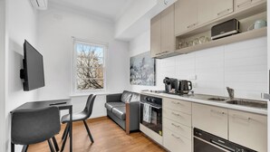 Una cucina moderna con forno a incasso, macchina da caffè e lavastoviglie. C'è un'area pranzo con tavolo e sedie, e un divano grigio.