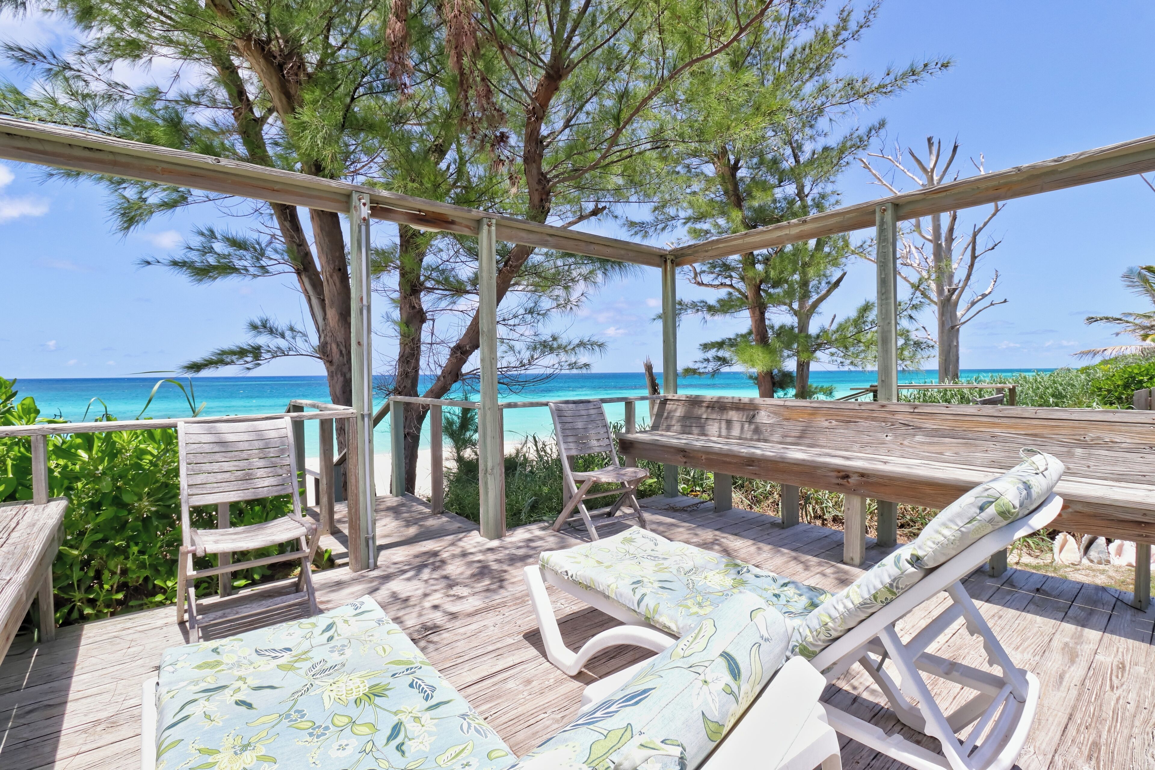 A wooden deck with lounge chairs and a table overlooking a beach.