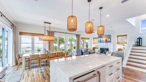 Une cuisine spacieuse dotée d’un grand îlot central, de planchers en bois et de luminaires suspendus en osier.