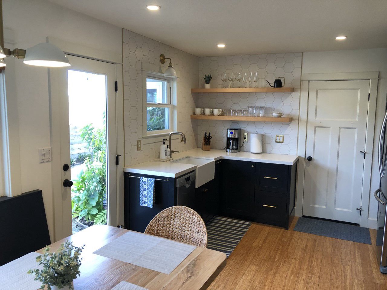 A compact kitchen with a dining area, a window with a view of greenery, and a door leading outside.