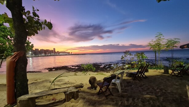 A beach with a sunset view, a sandy area with a bench, and a chair. - Pousada Meireles Praia (Fortaleza)
