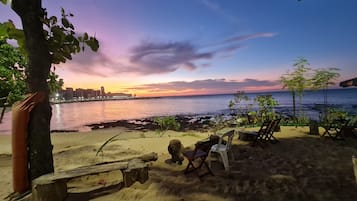 Uma praia com vista para o pôr do sol, uma área arenosa com um banco e uma cadeira.