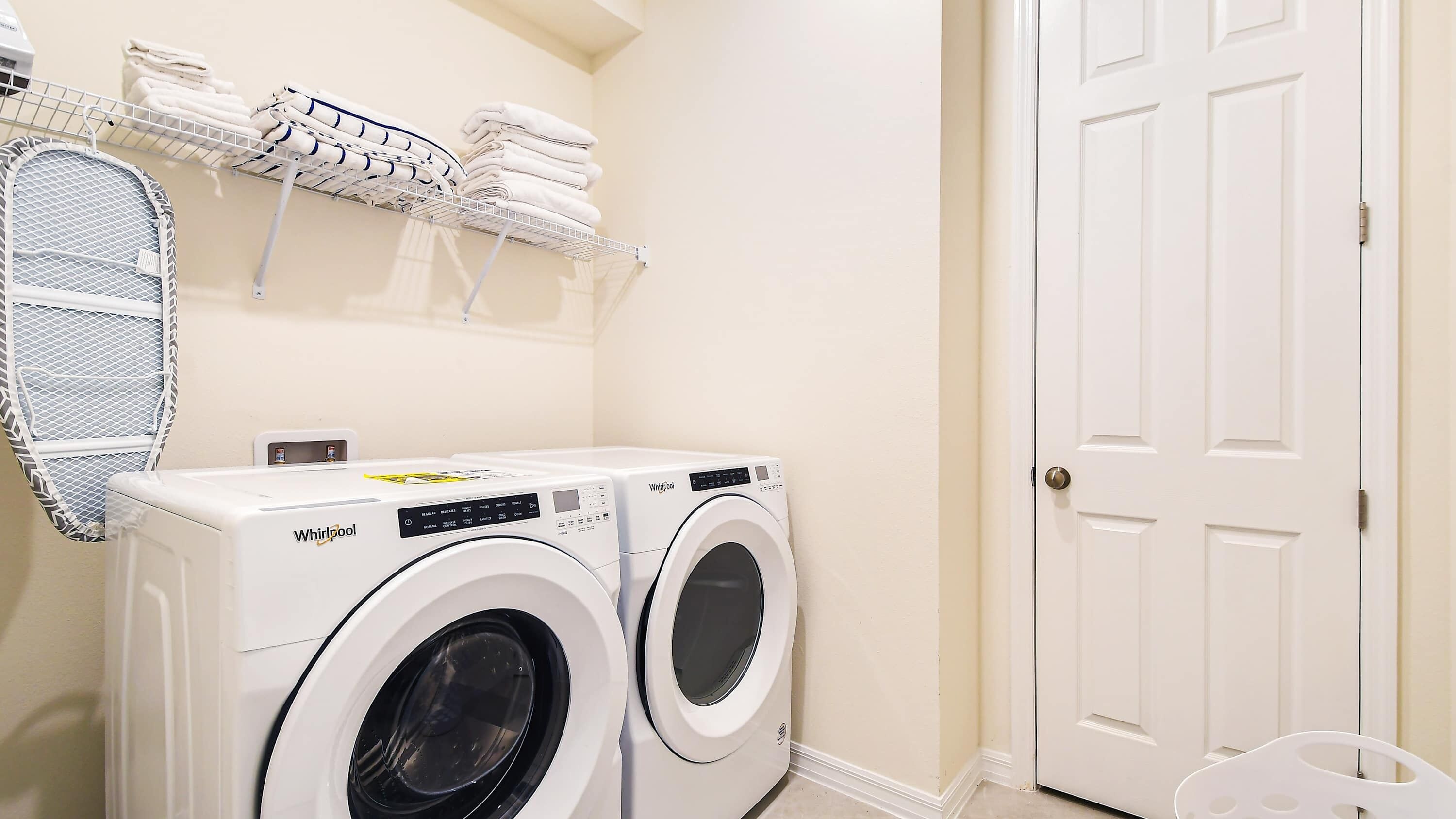 A laundry room with two Whirlpool front-loading washing machines, a drying rack with folded towels, and a white door.