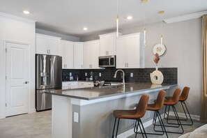 Cozinha moderna com armários brancos, eletrodomésticos de aço inoxidável, uma ilha grande com banquetas e iluminação pendente.