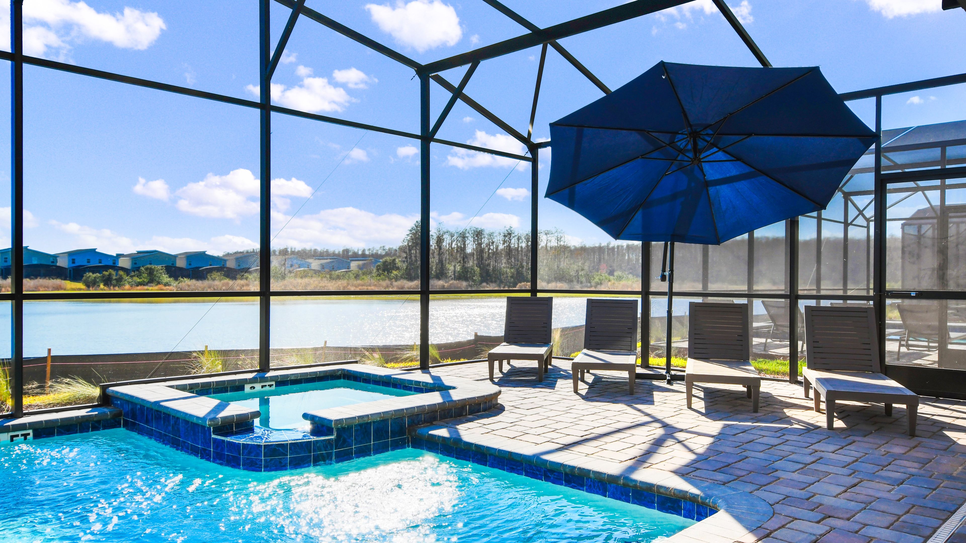 A pool area with a hot tub, lounge chairs, and a large umbrella.