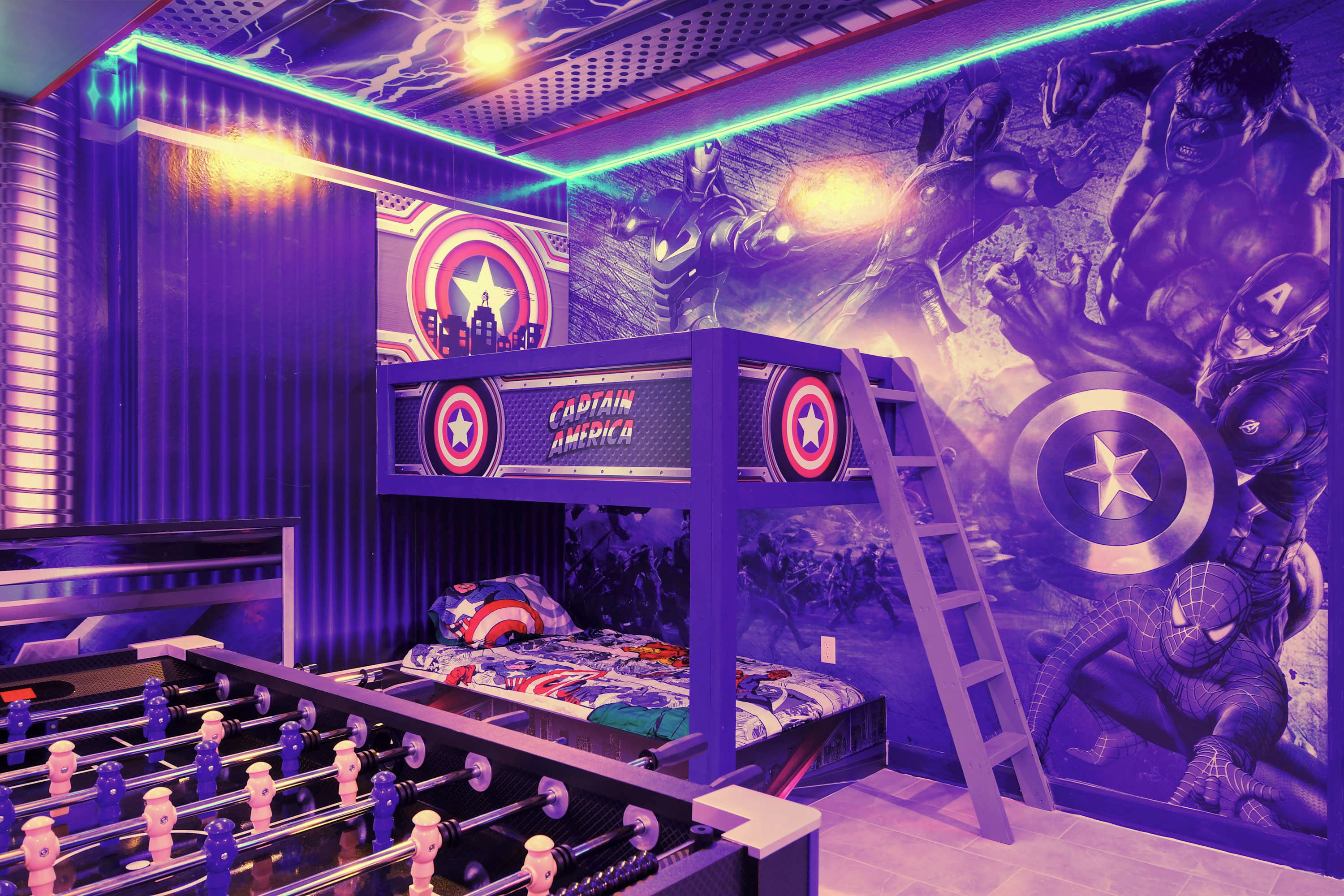 A room with a bunk bed, a foosball table, and a wall mural featuring superhero characters.