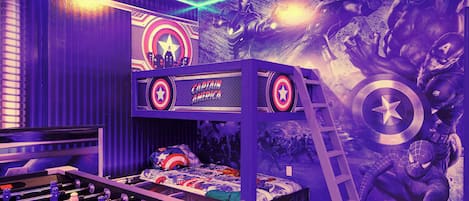 Una habitación con una cama litera, una mesa de fútbol de mesa y un mural en la pared con personajes de superhéroes.