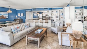 Una sala de estar moderna con un sofá, una mesa de centro y sillones. Hay una zona de cocina con electrodomésticos y una mesa de comedor.