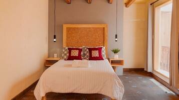 A neatly made bed with patterned pillows, a wooden headboard, and a small plant on a bedside table.