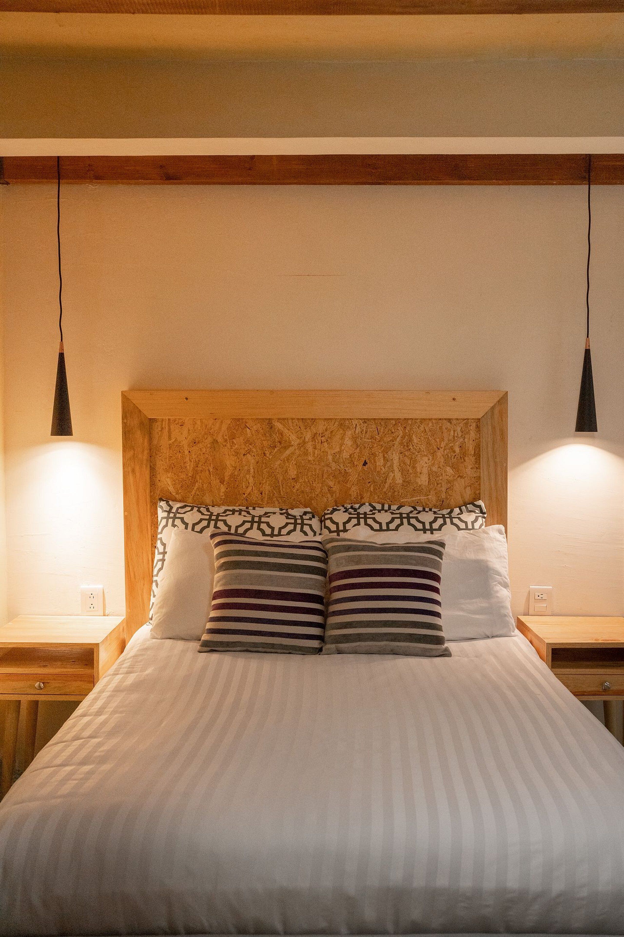 A bed with a wooden headboard, two bedside tables, and two pendant lights.