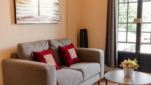 Un salón con sofá gris, cojines rojos, una mesita de centro redonda y un cuadro colgado en la pared de un árbol.