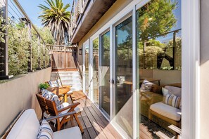 Une terrasse couverte avec une plateforme en bois, des sièges d’extérieur et des portes-fenêtres coulissantes donnant sur un jardin.