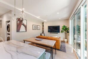 Un salon moderne avec un canapé, une table à manger, un téléviseur fixé au mur et une plante en pot.