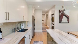 Una cocina moderna con armarios blancos, encimera de mármol y refrigerador de acero inoxidable.