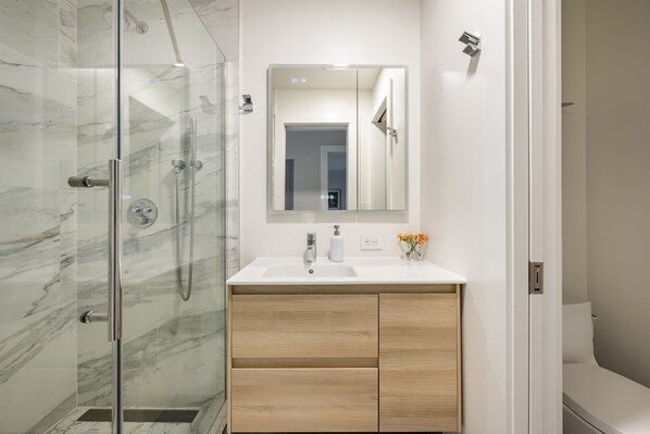 Une salle de bain moderne avec une douche en verre, un lavabo blanc avec un miroir au-dessus et des meubles en bois.