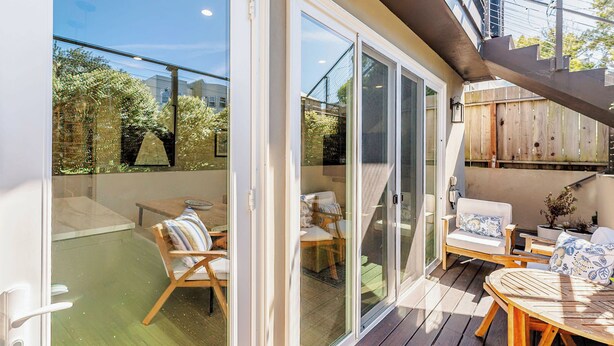 Un patio techado al aire libre con piso de madera, puertas correderas de vidrio y una zona de estar con sillas y una mesa.