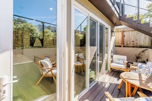Une terrasse extérieure couverte, dotée d’une plateforme en bois, de portes coulissantes en verre et d’un espace salon avec des chaises et une table.