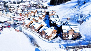 Ein schneebedecktes Resort mit mehreren Chaletgebäuden, einer Seilbahn und einem Berg im Hintergrund.