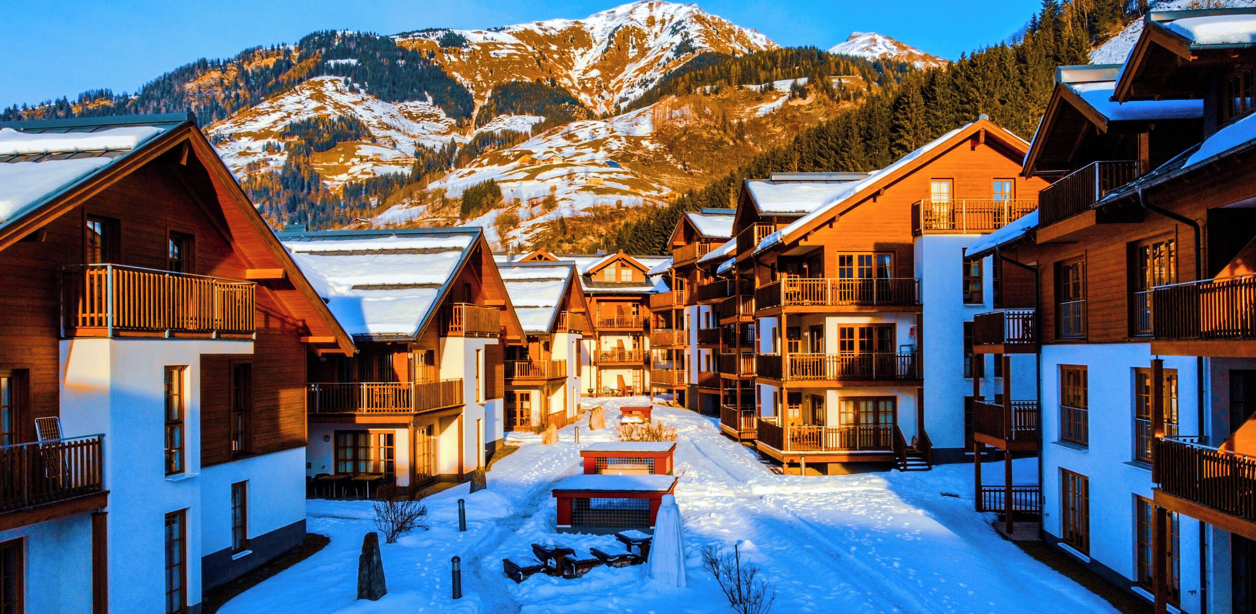 Un village enneigé, avec des bâtiments en bois, sur fond de montagnes.