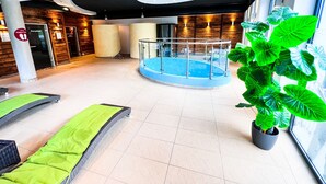 Ein moderner Innenpoolbereich mit Glasgeländer, grünen Sitzmöglichkeiten und Pflanzen in Töpfen.