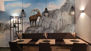Ein Restaurant mit Wandgemälde einer Berglandschaft und einer Sitzgelegenheit mit Tischen und Stühlen.