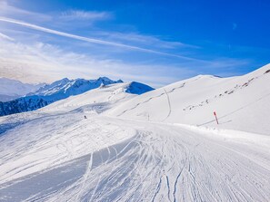 A snowy mountain slope with ski tracks and a clear sky.