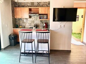 A compact kitchen with two bar stools, a flat-screen TV mounted on the wall, and a patterned backsplash. - Oh Baja California (San Cristóbal de las Casas)