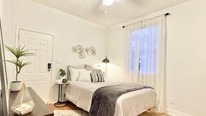 Ein Schlafzimmer mit Bett, Nachttisch, Lampe, Topfpflanze und Deckenventilator.