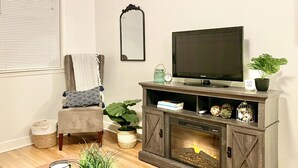 Ein Wohnzimmer mit Kamin, Fernseher, Sessel, Tisch und einer Topfpflanze.