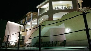 A building with a balcony overlooking a pool area, under a night sky with a visible moon. - Hotel Castello Budoni (Budoni)
