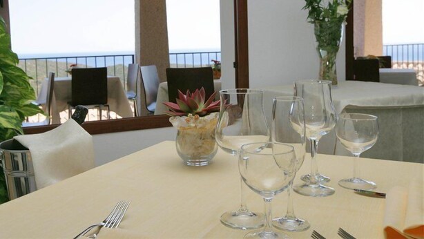 A table set for dining with a view of the sea, a potted plant, and a clear sky. - Hotel Castello Budoni (Budoni)