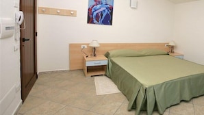 A hotel room with a bed, two bedside tables with lamps, a painting on the wall, a door, and a telephone on the wall. - Hotel Castello Budoni (Budoni)