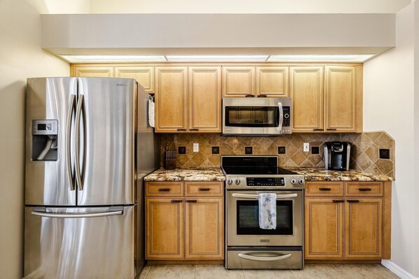 A compact kitchen with stainless steel appliances, wooden cabinets, and a tiled backsplash. - Southern exposure Pool, Gulf Access, - Villa Summer's Day - Roelens Vacations (Cape Coral)