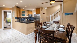 A kitchen with a central island, stainless steel appliances, and a dining area with a table set for four. - North Coast Village 3brm Penthouse - Amazing Oceanfront Panoramic Views -  G315 (Oceanside)