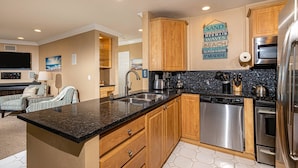 A kitchen with wooden cabinets, a granite countertop, stainless steel appliances, and a decorative wall sign. - North Coast Village 3brm Penthouse - Amazing Oceanfront Panoramic Views -  G315 (Oceanside)