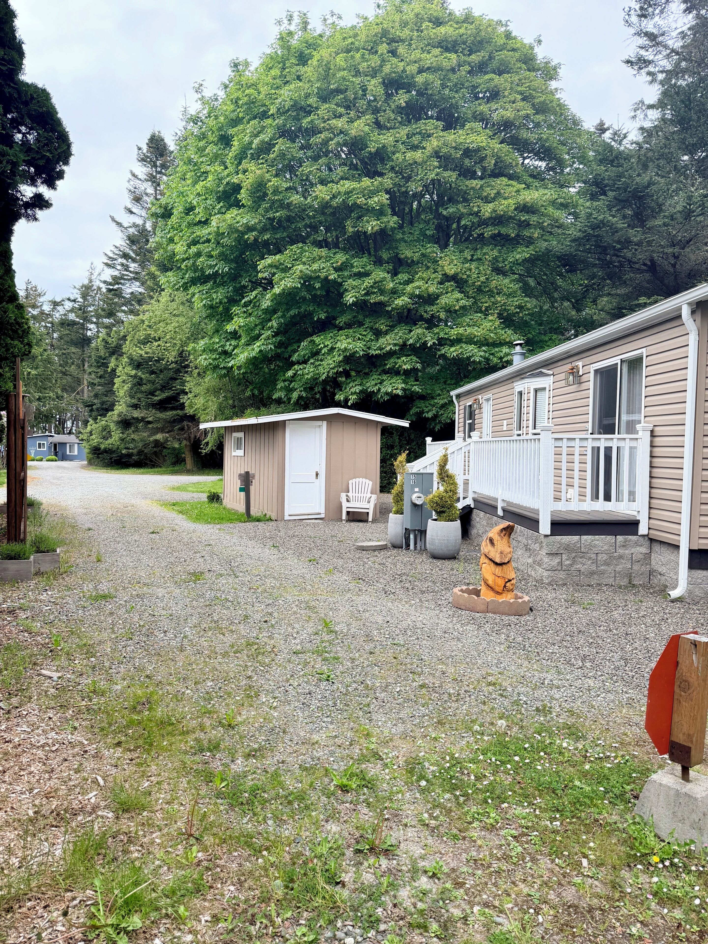 A gravel driveway leading to a mobile home with a small shed and a white chair.