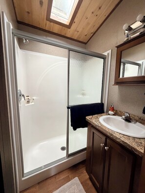 A modern bathroom with a glass-enclosed shower, a white sink, and a wooden vanity.