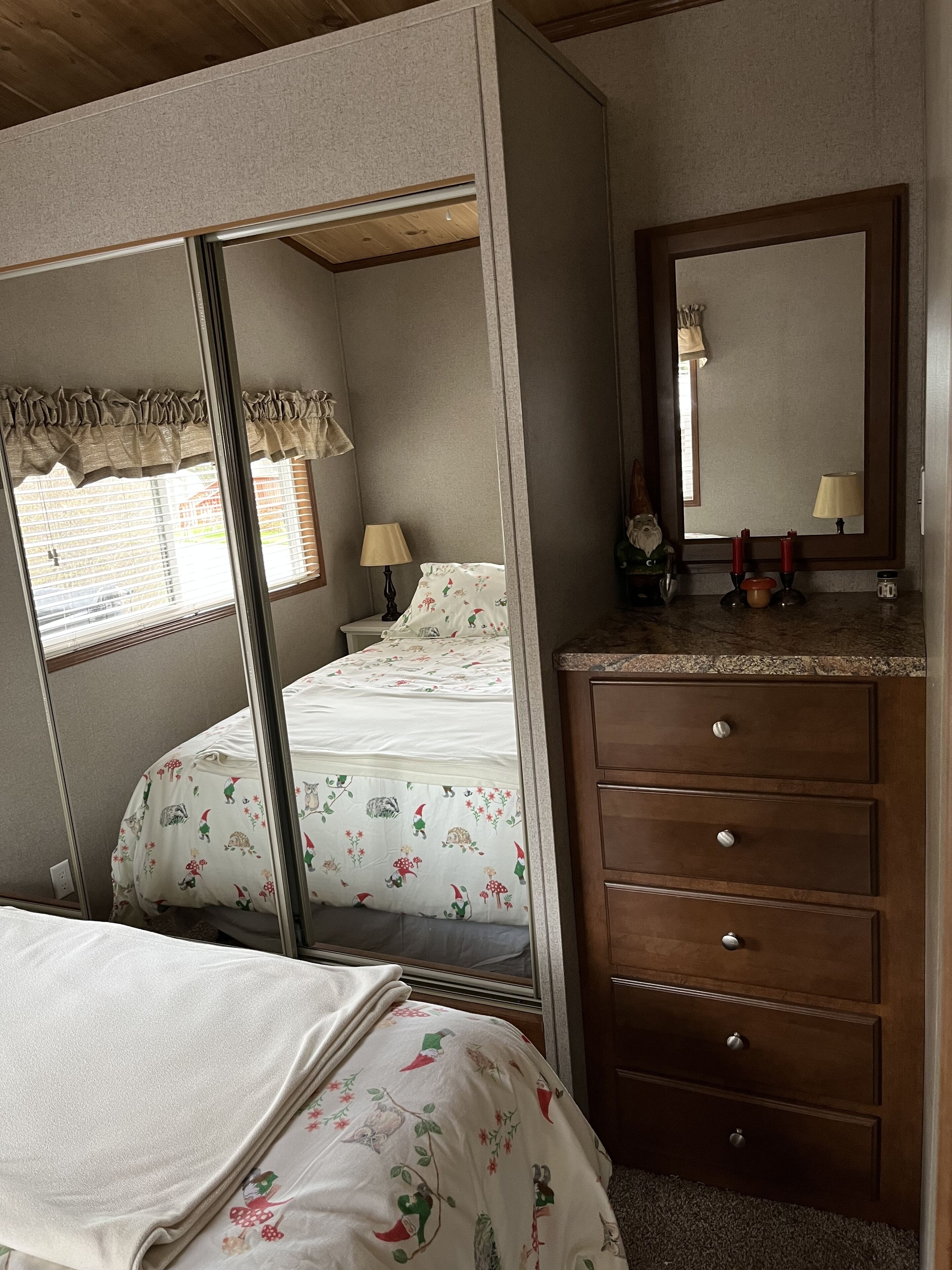 A bedroom with a bed, a dresser, a mirror, and a window with blinds.
