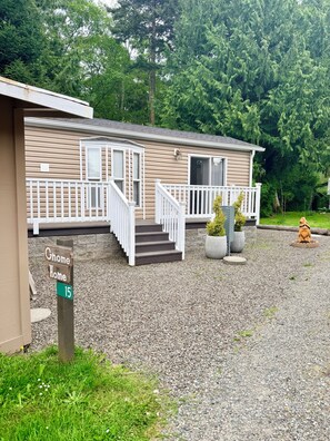 A single-story mobile home with a front porch, a gravel driveway, and a mailbox labeled 'Gnome Home 15'.
