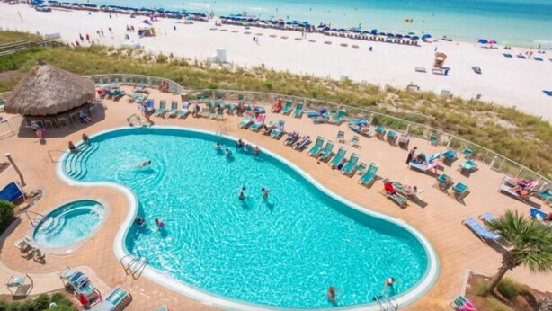 Una piscina grande con varias pistas, rodeada de sillas de descanso y una playa al fondo.