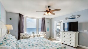 Un dormitorio con cama, ventilador de techo, televisor, cómoda y vista al océano.