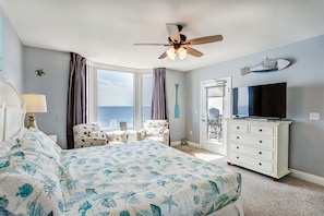 Ein Schlafzimmer mit Bett, Deckenventilator, Fernseher, Kommode und Blick auf den Ozean.